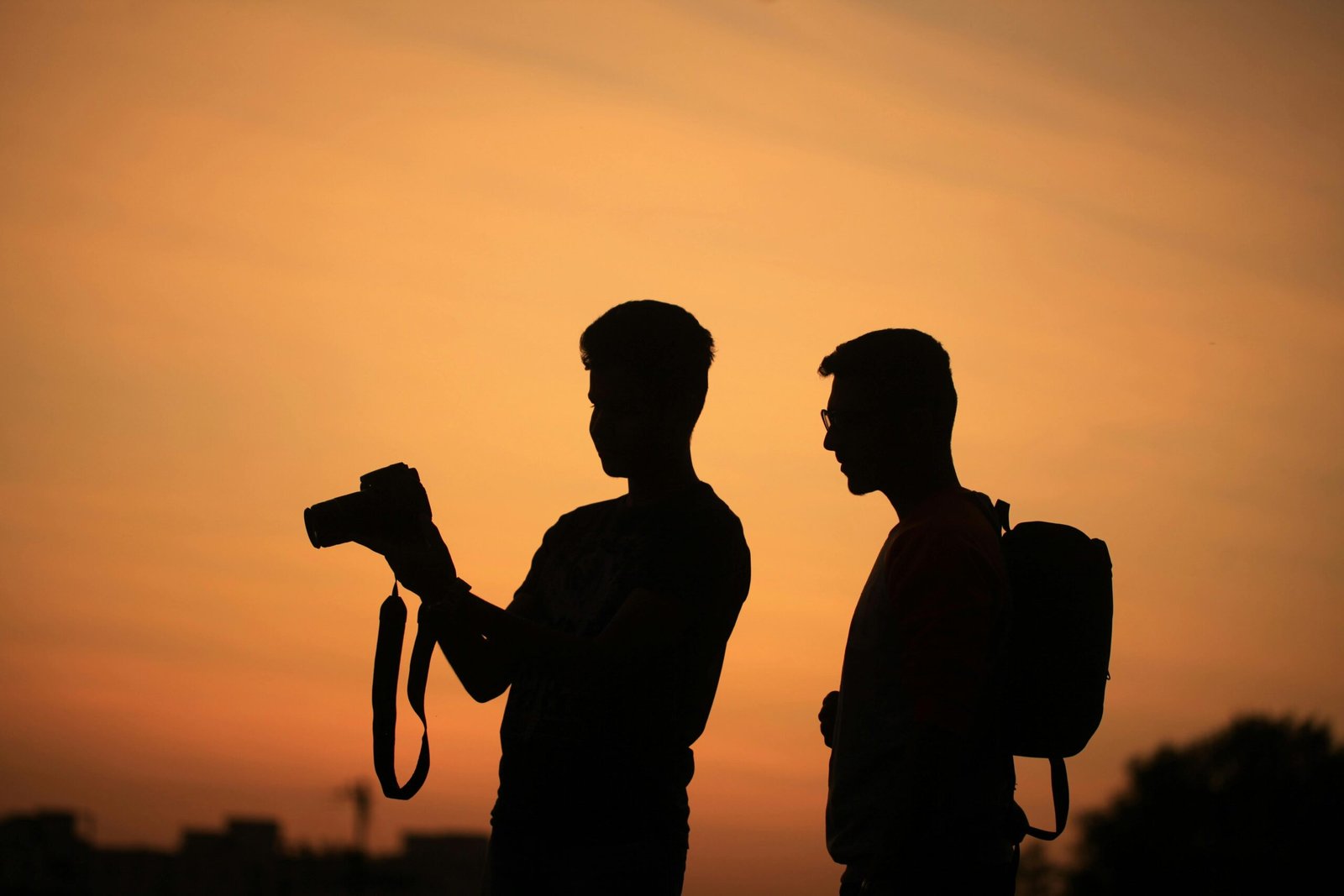 Two photographers silhouetted against a warm sunset sky, capturing serene moments.